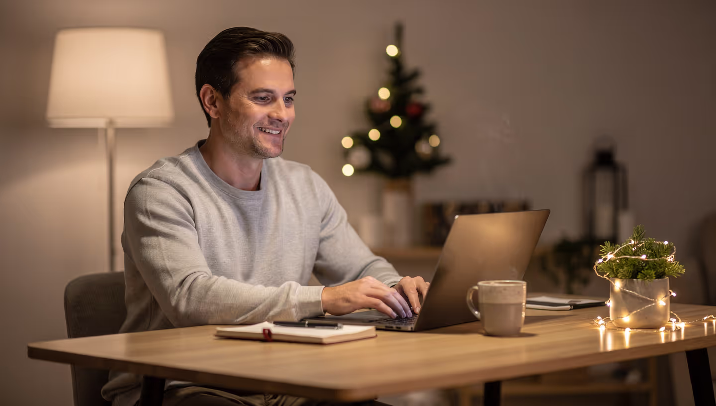 Small business owner calmly managing holiday customer support on laptop with seasonal decorations in background