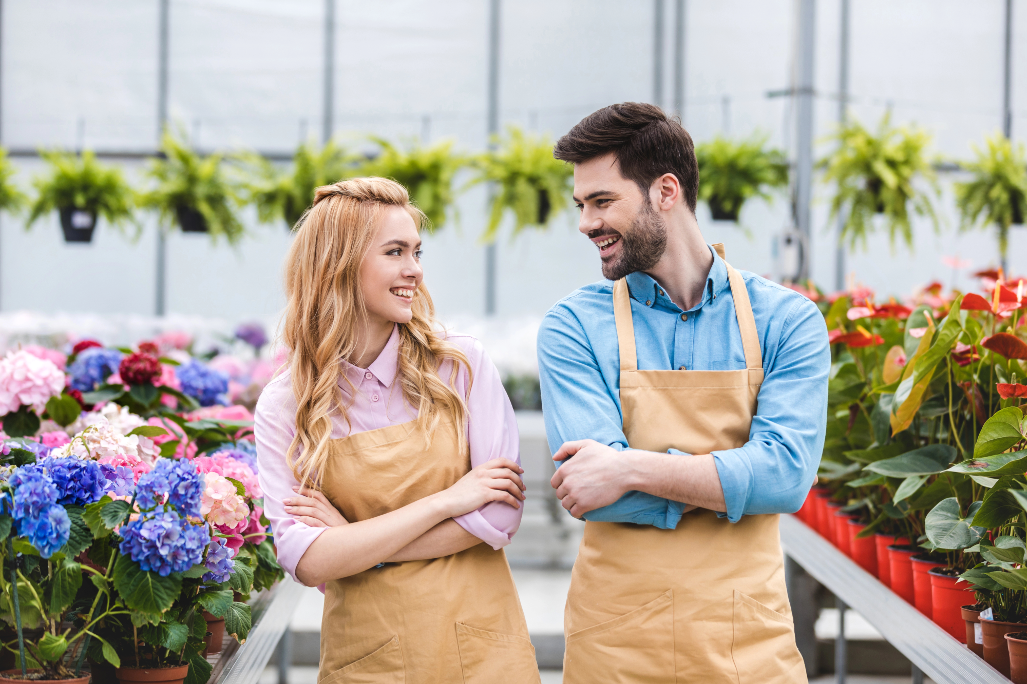  a woman with long blonde hair and a man with dark hair wear tan aprons, exuding a friendly atmosphere.