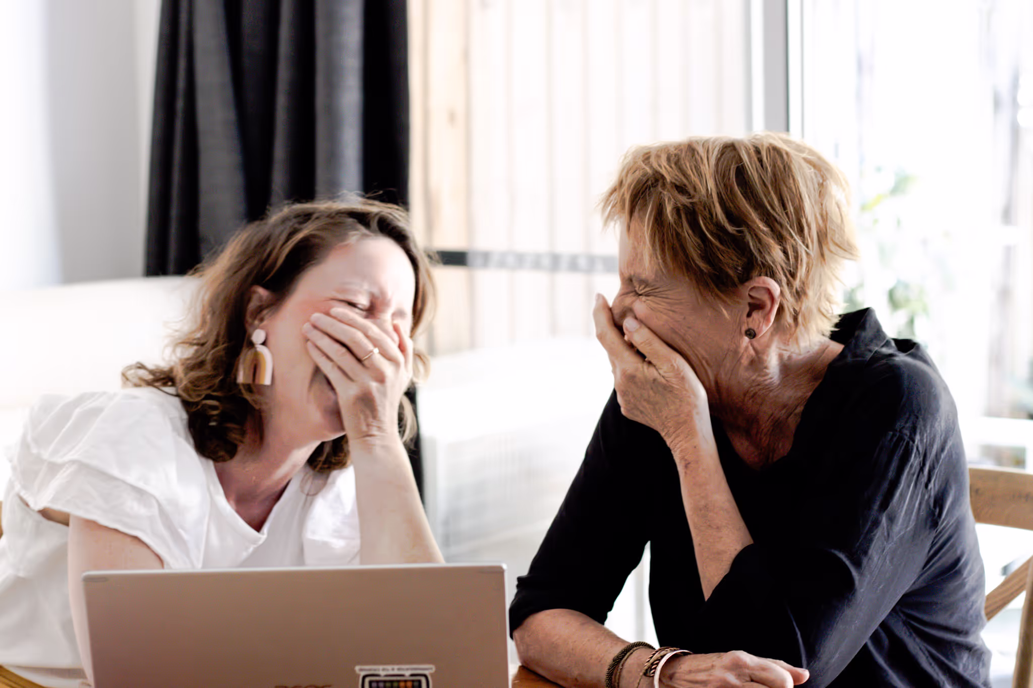 Hannah Lee-Archer and a client sharing a joyful moment, laughing together at a table with a laptop open, capturing the warmth and connection of carer support.