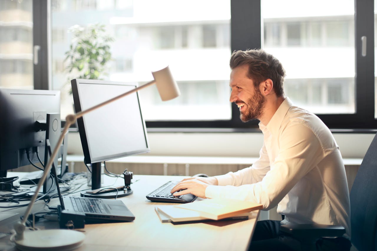 A man smiling happily while checking increased Amazon sales on his computer after using a long tail keywords strategy to improve SEO and performance