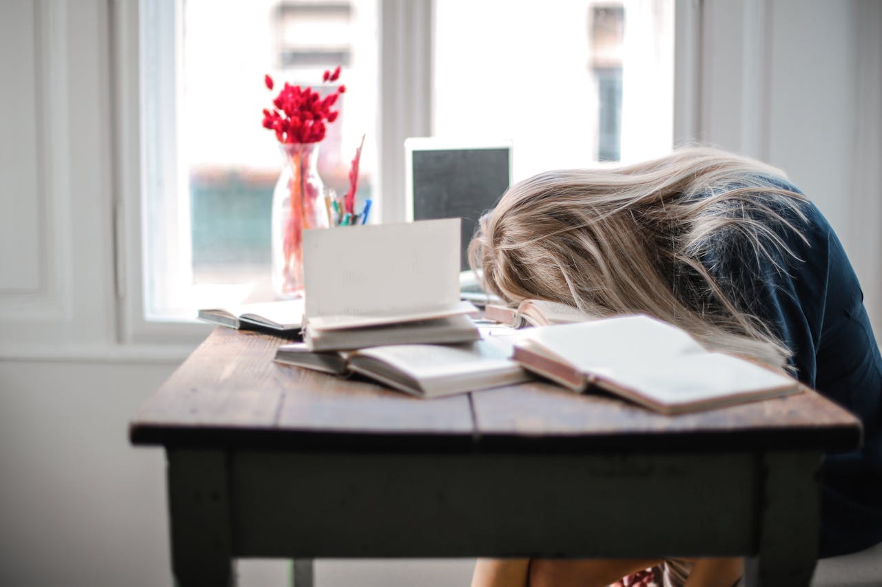 Stressed College Student Studying at Desk College student resting his head on a desk while studying, appearing stressed and overwhelmed, illustrating the importance of supporting college student mental health from distance.