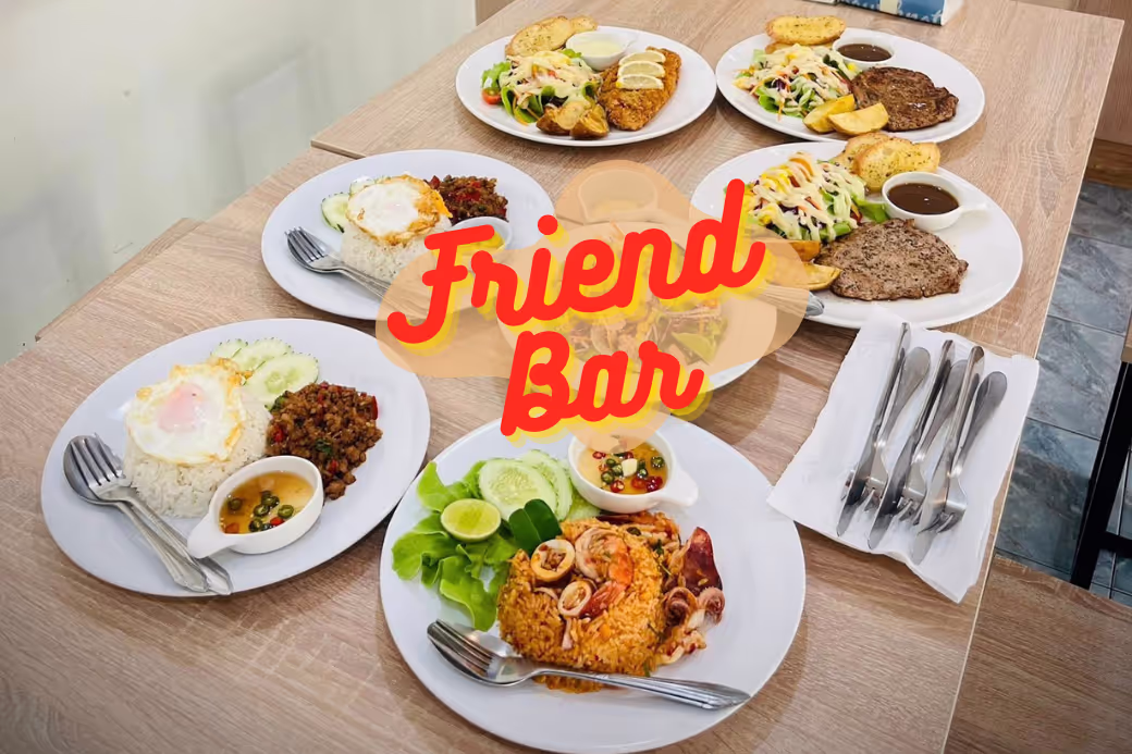 อาหารหลากหลายชนิด ทั้งพิซซ่า สเต็ก และอาหารไทย วางอยู่บนโต๊ะ ที่ Friend Bar บางสะพานน้อย
