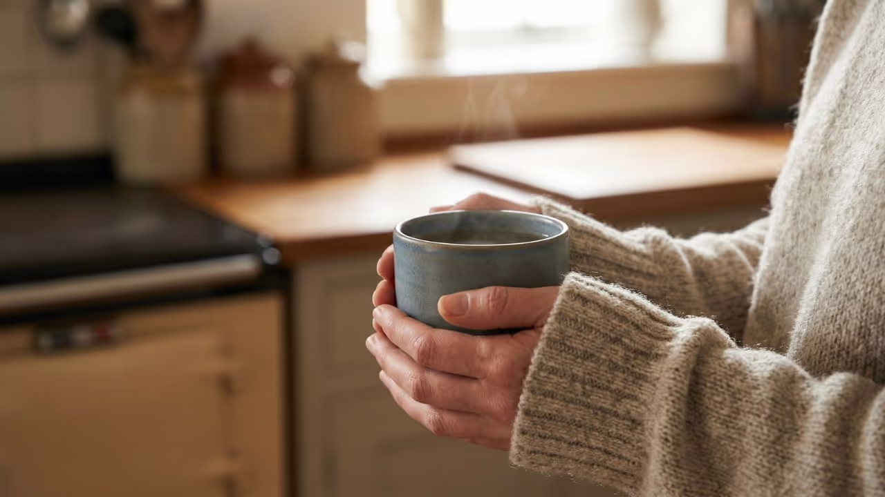 Hands wrapped warmly around a ceramic mug of tea in a quiet kitchen, highlighting the need for gentle, low-stress tools while tracking oxalates with chronic fatigue.