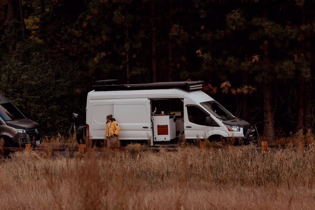 A smiling couple standing proudly next to their red T4 van, ready for a European adventure.