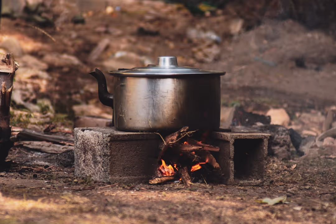 A hand holding a ceramic coffee mug by a crackling campfire at dawn, showing rustic charm.