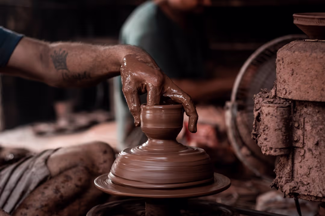A close-up image showing a hand pouring coffee from a vintage-style kettle, surrounded by rustic elements like leather and wood, emphasizing craftsmanship and heritage.
