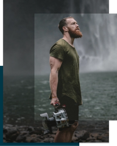 Man near waterfall posing with camera in hand