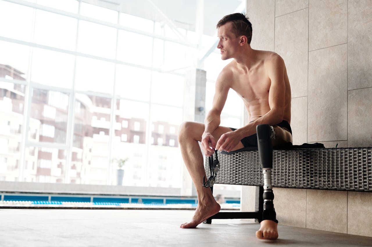 Young man with prosthetic leg sitting by a swimming pool preparing for a swim indoors